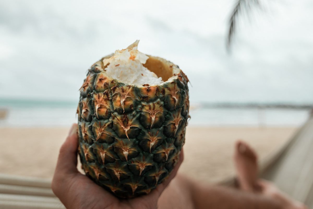A person holds a pineapple while reclining on a Puerto Rican beach.