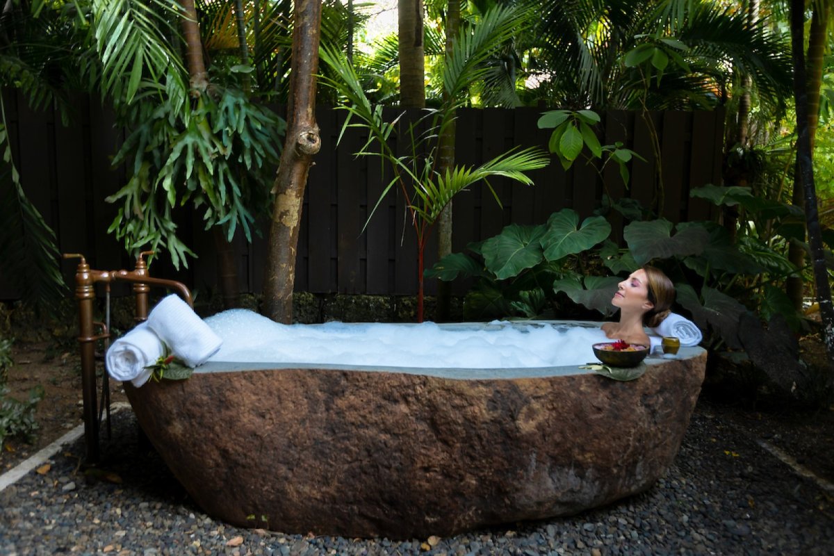 Una mujer se relaja en una bañera de piedra al aire libre en el Spa Botánico de Puerto Rico.